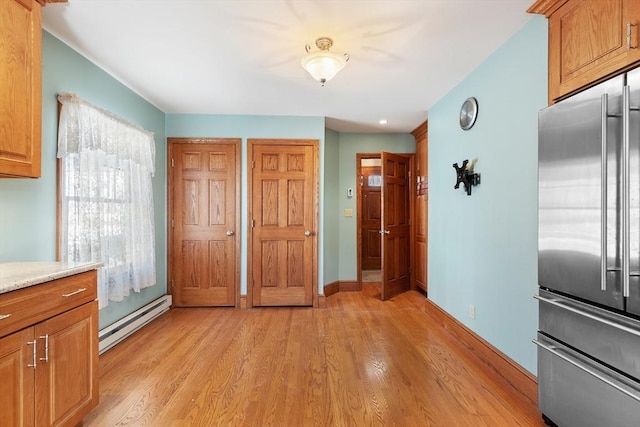 kitchen with light stone counters, high quality fridge, light hardwood / wood-style floors, and a baseboard heating unit