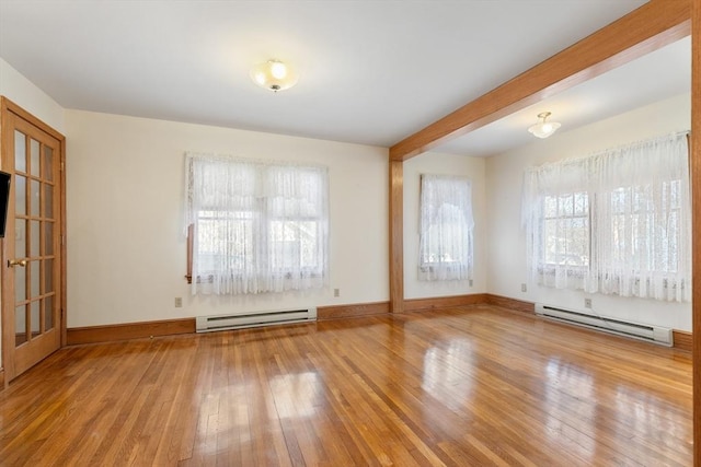 empty room featuring a healthy amount of sunlight, a baseboard heating unit, and hardwood / wood-style floors