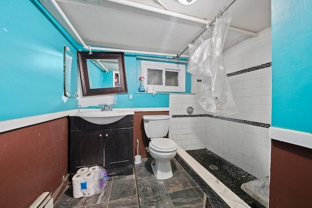 bathroom featuring toilet, baseboard heating, tiled shower, and vanity