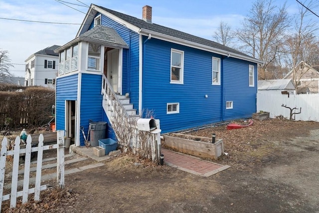 view of front of home featuring a shingled roof, a chimney, and fence