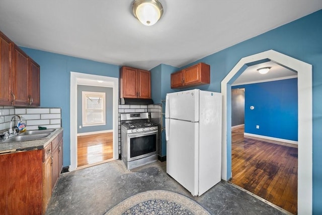 kitchen featuring a sink, stainless steel range with gas cooktop, freestanding refrigerator, and baseboards