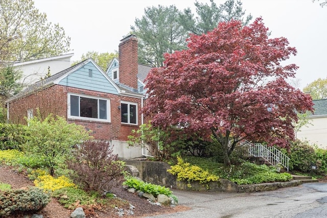 view of side of home featuring brick siding, a chimney, and stairs