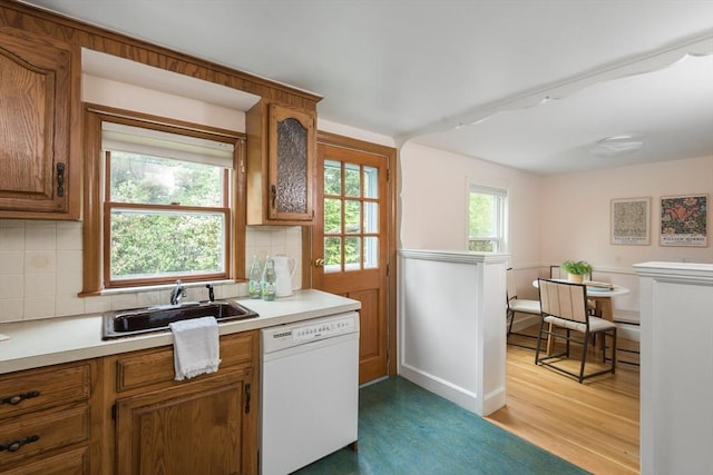 kitchen featuring dishwasher, a sink, light wood-style floors, brown cabinets, and light countertops