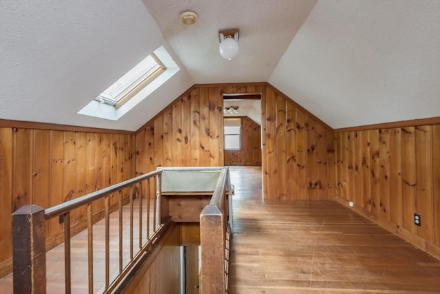 bonus room featuring a skylight, hardwood / wood-style flooring, a textured ceiling, vaulted ceiling, and wood walls