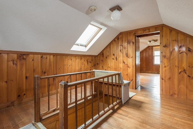 bonus room featuring a skylight, lofted ceiling, light wood finished floors, wood walls, and a textured ceiling