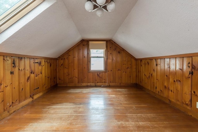 additional living space featuring light wood-type flooring, vaulted ceiling, a textured ceiling, and wood walls