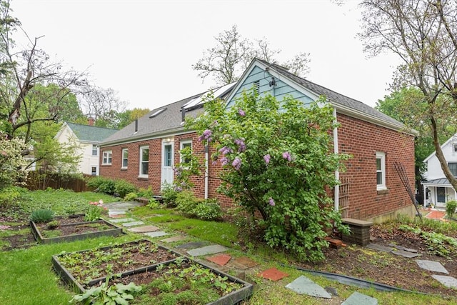 rear view of property featuring a garden, brick siding, and fence