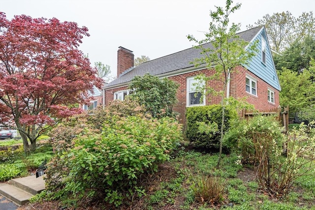 view of property exterior with a chimney, brick siding, and roof with shingles