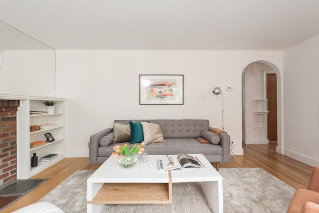 living room featuring arched walkways, light wood-style floors, and baseboards