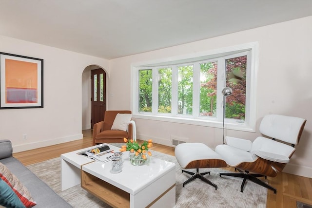 living area with arched walkways, baseboards, and light wood finished floors