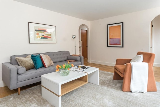 living room with arched walkways, light wood finished floors, and baseboards