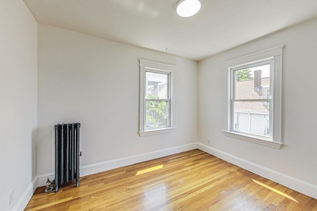 spare room featuring radiator heating unit, wood-type flooring, and a wealth of natural light