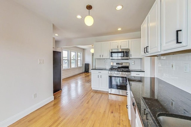 kitchen with appliances with stainless steel finishes, white cabinetry, dark stone countertops, light hardwood / wood-style floors, and decorative light fixtures