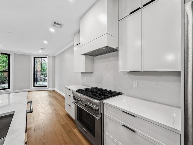 667 Tremont St Unit 2, Boston, MA 02118 - kitchen with stainless steel range, white cabinetry, light wood-style flooring, custom range hood, and recessed lighting