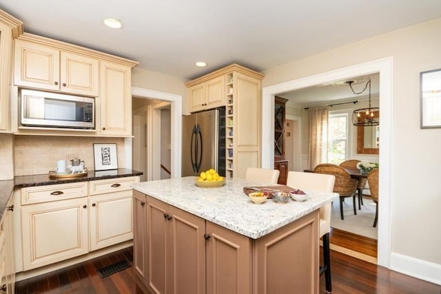 kitchen with appliances with stainless steel finishes, cream cabinets, a kitchen island, and dark wood-style floors