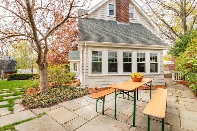 exterior space with a shingled roof and a patio area