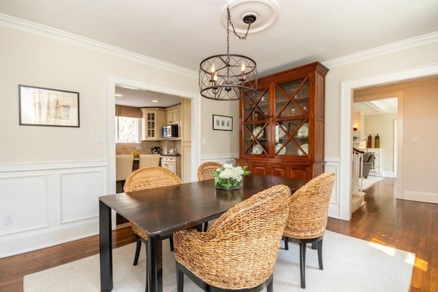 dining space featuring an inviting chandelier, ornamental molding, a decorative wall, and wood finished floors