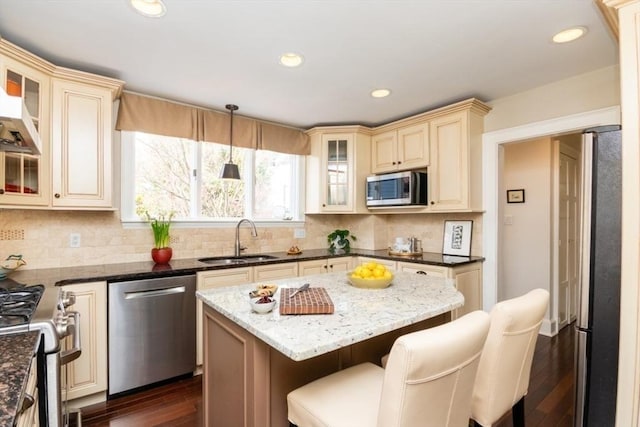 kitchen featuring appliances with stainless steel finishes, a sink, dark stone counters, cream cabinetry, and a kitchen bar