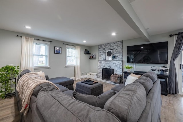 living area with beamed ceiling, a stone fireplace, recessed lighting, and wood finished floors