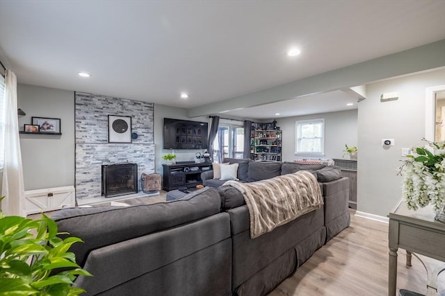living room with a stone fireplace, recessed lighting, light wood finished floors, and baseboards