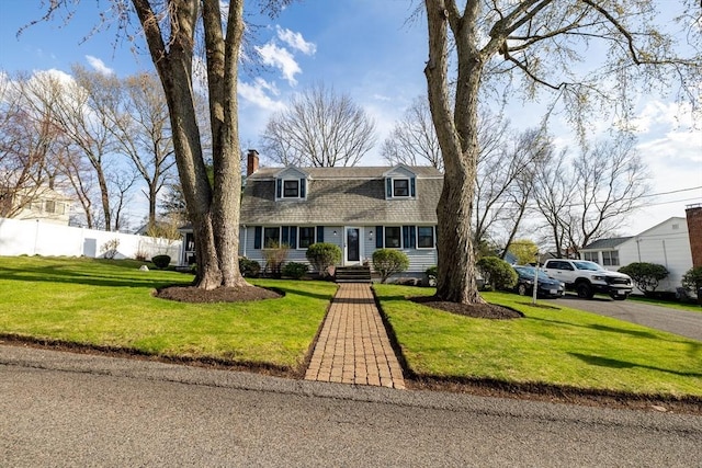 new england style home with roof with shingles, fence, a front yard, and a chimney