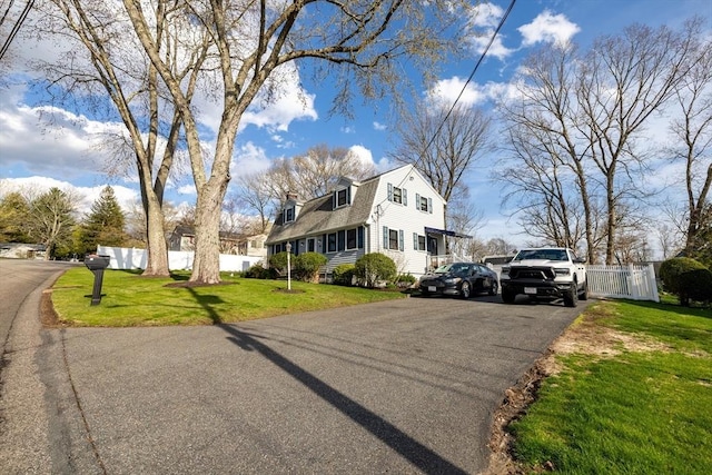 view of front of house with fence, a chimney, a front yard, and aphalt driveway