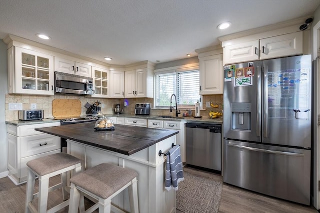 kitchen with appliances with stainless steel finishes, wood finished floors, a sink, glass insert cabinets, and a breakfast bar