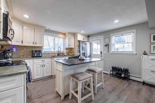 kitchen with wood finished floors, a breakfast bar area, white cabinets, a sink, and stainless steel appliances
