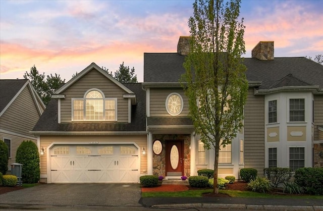 traditional home featuring driveway, roof with shingles, a garage, and a chimney