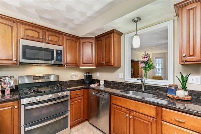 kitchen with stainless steel appliances, a sink, brown cabinetry, and dark stone countertops