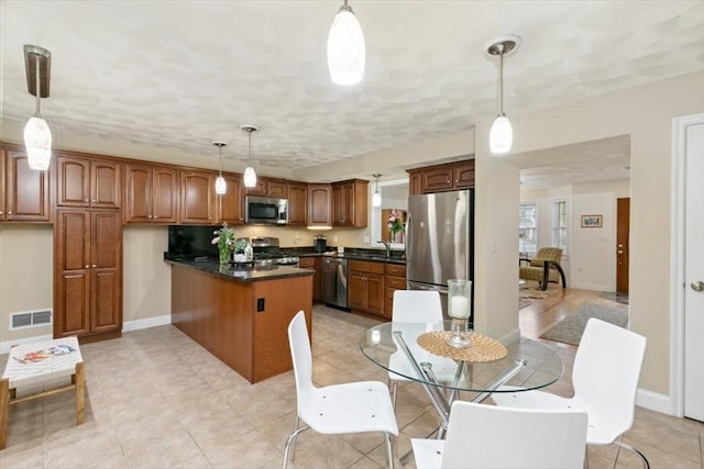 kitchen with appliances with stainless steel finishes, dark countertops, a peninsula, brown cabinets, and a sink