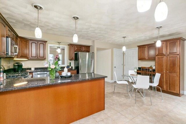 kitchen featuring appliances with stainless steel finishes, dark stone countertops, a peninsula, and pendant lighting