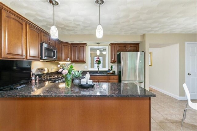 kitchen featuring appliances with stainless steel finishes, pendant lighting, a peninsula, and dark stone counters