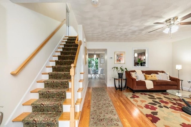 staircase featuring a ceiling fan, wood finished floors, baseboards, and a textured ceiling