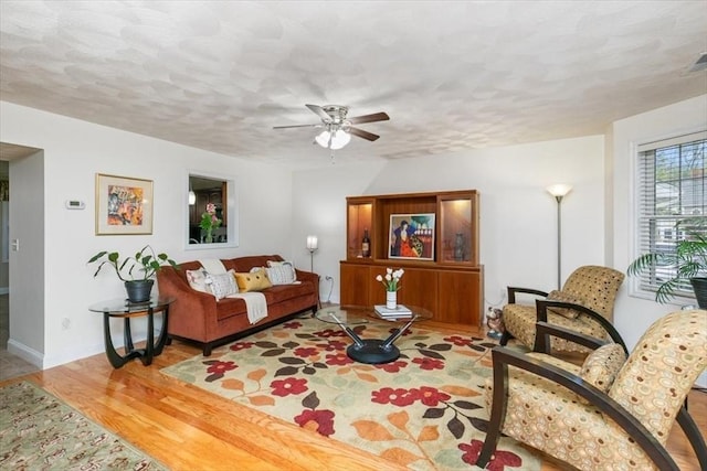 living room with wood finished floors, ceiling fan, a textured ceiling, and baseboards