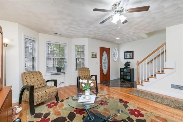 living area featuring wood finished floors, ceiling fan, stairway, and baseboards