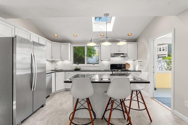 kitchen with stainless steel appliances, under cabinet range hood, a skylight, a sink, and vaulted ceiling