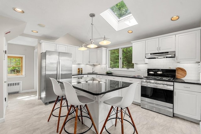 kitchen featuring stainless steel appliances, under cabinet range hood, radiator heating unit, a skylight, and backsplash