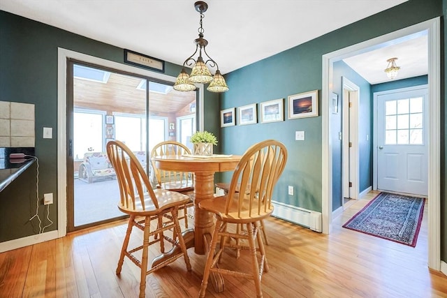 dining area with a baseboard heating unit, light wood finished floors, and baseboards