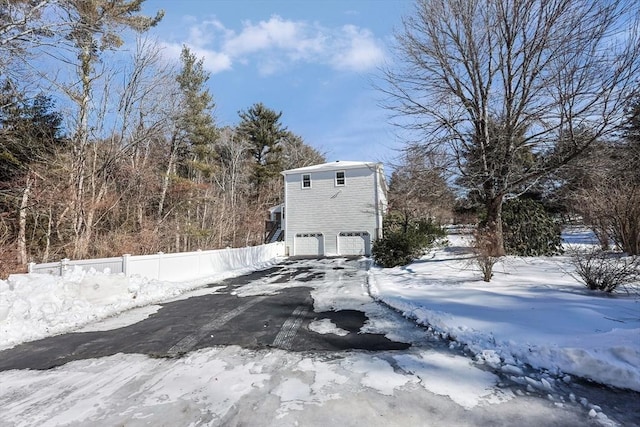 view of snowy exterior with aphalt driveway, an attached garage, and fence