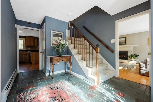 stairs with stone tile floors, a fireplace, a baseboard heating unit, and baseboards