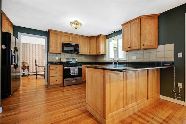 kitchen with a peninsula, light wood-type flooring, black appliances, dark countertops, and pendant lighting