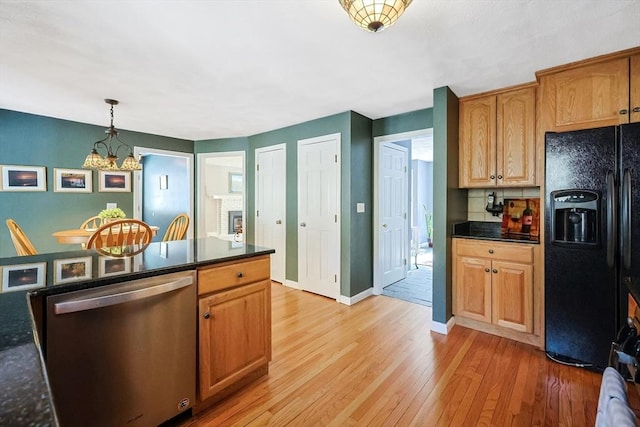 kitchen featuring light wood finished floors, dishwasher, black fridge with ice dispenser, dark countertops, and decorative light fixtures