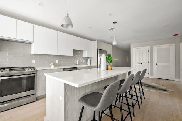 kitchen with light hardwood / wood-style floors, a kitchen island, decorative light fixtures, stainless steel appliances, and white cabinetry