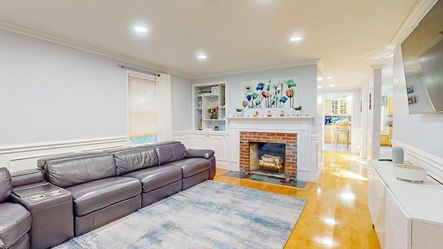 living room with built in shelves, light hardwood / wood-style flooring, ornamental molding, and a fireplace