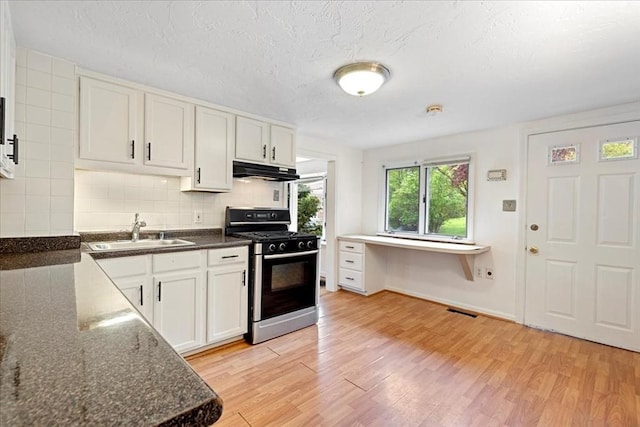 kitchen with stainless steel gas range oven, a sink, under cabinet range hood, light wood-style floors, and a textured ceiling
