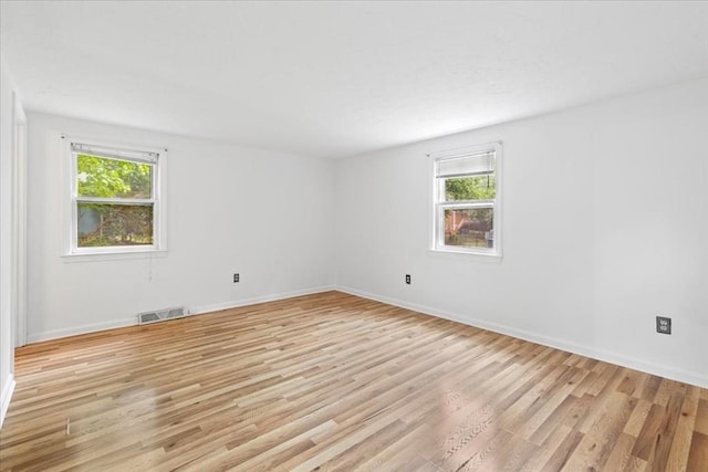 empty room featuring plenty of natural light, light wood-style floors, and baseboards