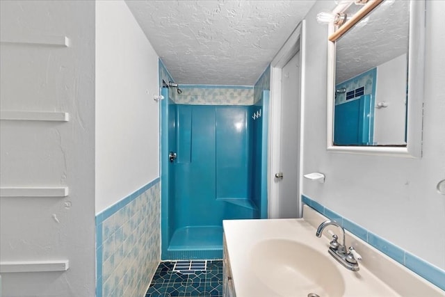 bathroom featuring a textured ceiling, a shower, vanity, tile walls, and tile patterned floors