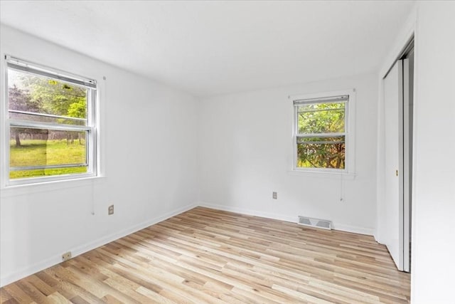 unfurnished bedroom with multiple windows, light wood-style floors, and baseboards