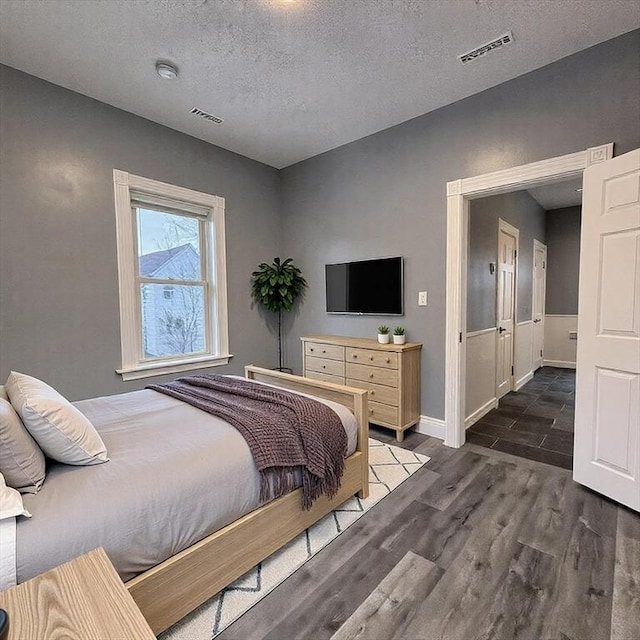 bedroom featuring baseboards, visible vents, dark wood finished floors, and a textured ceiling